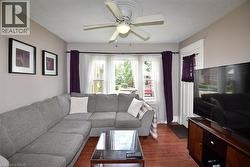 Living area featuring wood-finish flooring, a ceiling fan with light fixture, multiple windows with white trim, and a white paneled door with decorative trim - 