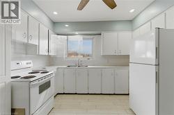 Kitchen featuring white cabinetry, white appliance suite, white subway tile backsplash, light-toned countertops, and wood-finish flooring - 