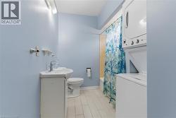 Bathroom featuring a corner vanity with integrated sink, toilet, tub with shower, and stacked laundry appliances - 