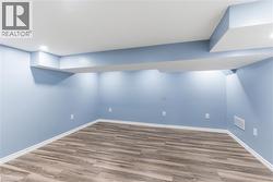 Finished lower level with wood-finish flooring, light blue walls, recessed lighting, and white baseboards - 