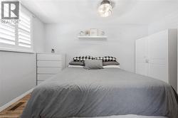 Bedroom featuring white wall paint, window with white plantation shutters, wood-finish flooring, built-in ceiling light fixture, and a white storage dresser - 