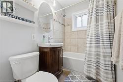 Bathroom featuring a wood-finish vanity with a rectangular basin sink, a circular wall-mounted mirror, and a white toilet - 