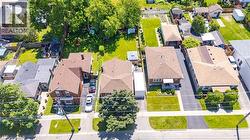 Aerial perspective showcasing a residential street with multiple properties, featuring paved driveways, green lawns, and mature trees - 