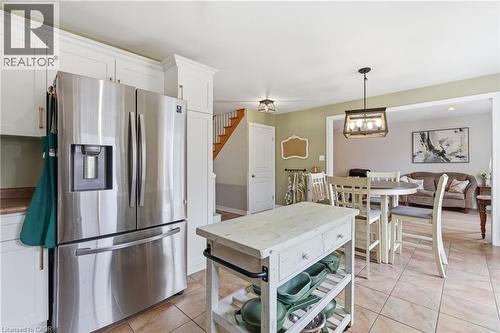 Kitchen featuring a stainless steel French door refrigerator, white cabinetry with gold-tone hardware, and tile flooring - 84 Duncairn Crescent, Hamilton, ON 