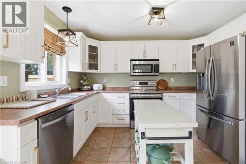 Well-appointed kitchen featuring white cabinetry, stainless steel appliances, a center island, warm-toned countertops, and tile flooring - 84 Duncairn Crescent, Hamilton, ON 