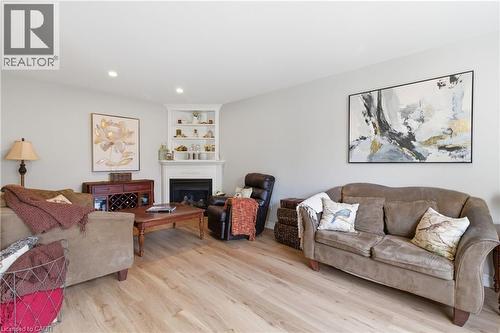 Living area featuring wood-finish flooring, recessed lighting, a fireplace with a white mantel, and built-in corner shelving - 84 Duncairn Crescent, Hamilton, ON 