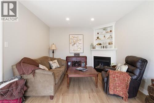 Living area featuring a corner fireplace with a white mantel and integrated shelving, light wood-finish flooring, recessed lighting, and neutral wall tones - 84 Duncairn Crescent, Hamilton, ON 
