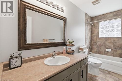 Bathroom featuring a single vanity with an integrated sink, a rectangular framed mirror, a three-bulb vanity light, and a tub/shower combination with a glass block window - 84 Duncairn Crescent, Hamilton, ON 