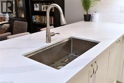Kitchen island featuring a stainless steel undermount sink, a gooseneck faucet, light-toned countertops, and paneled cabinetry with hardware - 