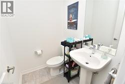 Pedestal sink with chrome faucet, a toilet, large wall-mounted mirror, and light-toned tile flooring - 