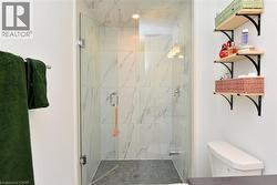 Glass-enclosed shower featuring white marble-look wall tiling, a rain shower head, and stone mosaic flooring - 