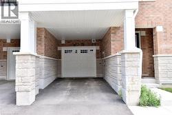 Covered carport entry featuring a white garage door with windows, brick facade, stone accents, white columns, and a beadboard ceiling - 