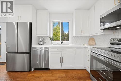 Modern kitchen featuring white shaker-style cabinetry, stainless steel appliances, a hexagonal tile backsplash, and wood-finish flooring - 1376 Royal Drive, Burlington, ON 