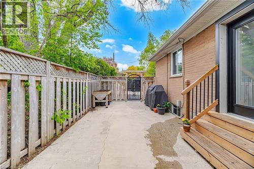 Private concrete patio featuring a wood privacy fence with lattice top, a black metal gate, and a brick exterior with a wood deck and handrail - 1376 Royal Drive, Burlington, ON 