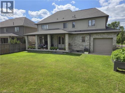 Expansive backyard featuring a large green lawn, covered patio with stone pillars, and a built-in garden bed - 2719 Torrey Pines Way, London, ON 
