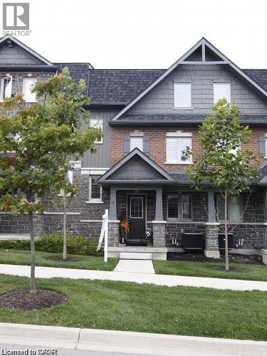 Townhome exterior featuring brick and stone cladding, a covered front porch, dark-framed windows, and a classic shingle roof - 4 Isaiah Drive, Kitchener, ON 