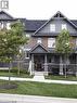 Townhome exterior featuring brick and stone cladding, a covered front porch, dark-framed windows, and a classic shingle roof - 4 Isaiah Drive, Kitchener, ON 