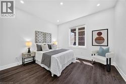 Bright bedroom featuring dark wood-finish flooring, white baseboards, and recessed lighting - 