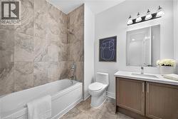Bathroom featuring a built-in bathtub with floor-to-ceiling tile surround, a single vanity with wood-finish cabinetry and white countertop, a rectangular mirror, and a four-light vanity fixture - 