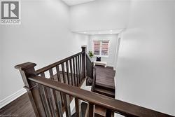 Staircase featuring dark wood-finish handrails and balusters, leading to an area with recessed lighting, a window with blinds, and wood-finish flooring - 