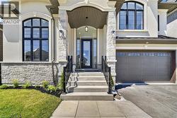 Stately stucco and stone facade featuring an arched entry, prominent black-framed windows, a dark paneled garage door with upper lites, and a concrete paver walkway leading to stone steps with wrought - 