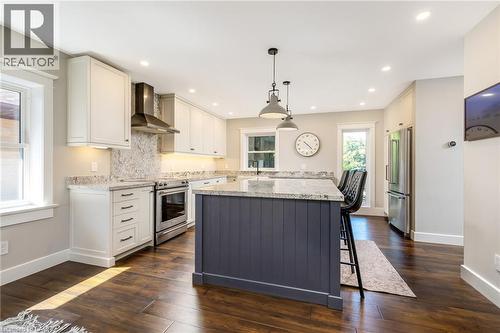 Modern kitchen featuring a central island with a granite countertop, white shaker-style cabinetry, stainless steel appliances, wood-finish flooring, and recessed lighting - 23 Mackenzie Drive, Georgetown, ON 