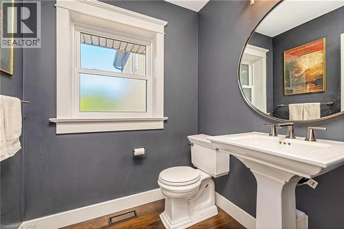 Powder room featuring a pedestal sink with brushed nickel fixtures, a round mirror, and a single-pane window with white trim - 23 Mackenzie Drive, Georgetown, ON 
