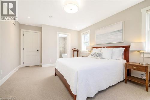 Spacious bedroom featuring light neutral wall tones, plush carpet flooring, a contemporary flush mount ceiling light, and an en-suite bathroom with a white rectangular tub and tiled walls - 23 Mackenzie Drive, Georgetown, ON 