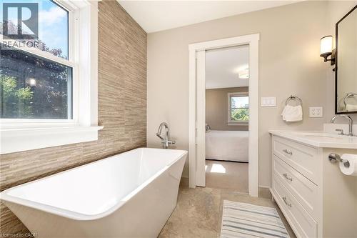 Bathroom featuring a freestanding soaking tub, wood-finish accent wall, single vanity with white cabinetry, polished chrome fixtures, and a framed mirror with wall sconces - 23 Mackenzie Drive, Georgetown, ON 