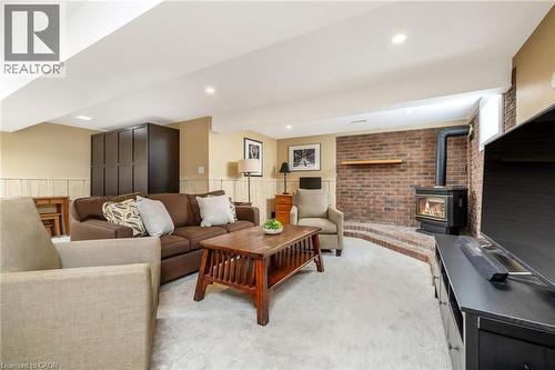 Spacious living area featuring a wood-burning stove with a brick surround, carpet flooring, recessed lighting, and wainscoting - 23 Mackenzie Drive, Georgetown, ON 