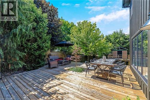 Expansive wood-plank deck featuring multiple zones for outdoor living, bordered by mature trees and a privacy fence - 23 Mackenzie Drive, Georgetown, ON 