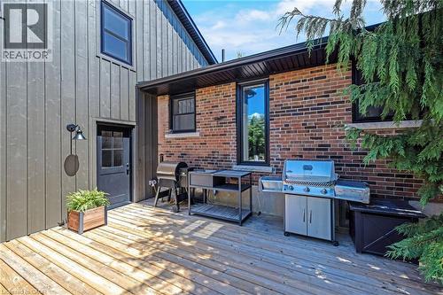 Expansive outdoor deck featuring wood flooring, board and batten siding, brick exterior, dark-framed windows, and a black exterior door with glass panes - 23 Mackenzie Drive, Georgetown, ON 