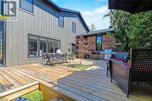 Multi-level wood deck featuring a built-in planter, brick exterior with an integrated outdoor kitchen, board and batten siding, and large sliding glass doors - 23 Mackenzie Drive, Georgetown, ON 