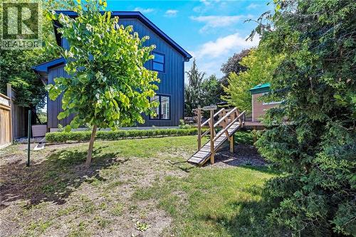Expansive outdoor area featuring a modern dark-paneled exterior, green lawn, established trees, a raised deck, and a wooden ramp structure - 23 Mackenzie Drive, Georgetown, ON 