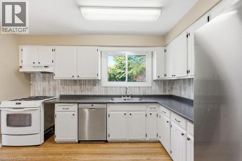 Kitchen featuring white cabinetry, wood-finish flooring, a stainless steel dishwasher, a double basin sink, and a large window - 14 Gateway Drive, Guelph, ON 