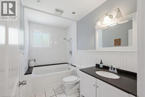 White bathroom featuring a built-in tub with black surround, a white vanity with a dark countertop and undermount sink, white subway tile shower walls, and beadboard wainscoting - 14 Gateway Drive, Guelph, ON 