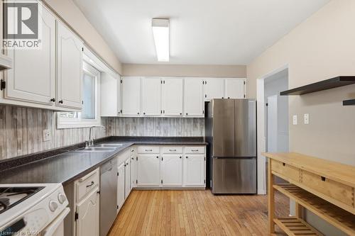 Kitchen featuring white cabinetry, dark countertops, wood-finish flooring, stainless steel appliances, and a window above the sink - 14 Gateway Drive, Guelph, ON 