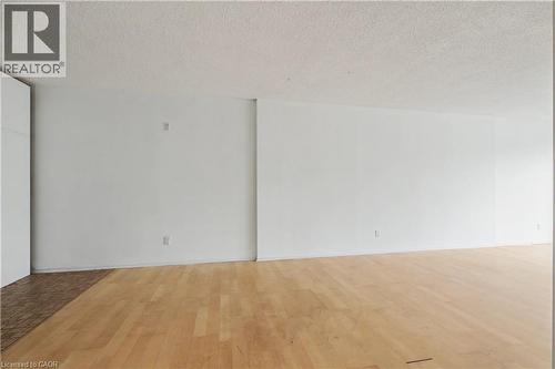 Spacious interior featuring light wood-finish flooring, white painted walls, and an acoustic ceiling finish - 175 Hunter Street E Unit# 401, Hamilton, ON - Indoor Photo Showing Other Room