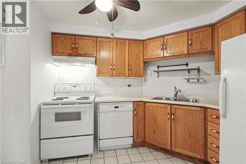 Kitchen featuring wood-finish cabinetry and white appliances, including a range, dishwasher, and refrigerator - 175 Hunter Street E Unit# 401, Hamilton, ON - Indoor Photo Showing Kitchen With Double Sink