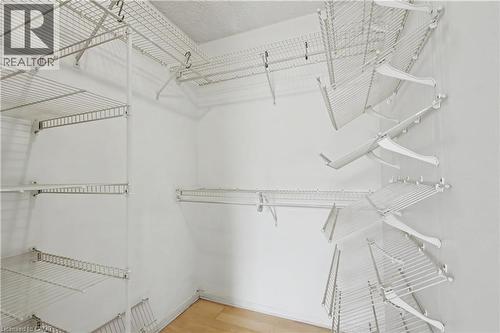 Walk-in closet featuring white wire shelving, multiple hanging rods, and light wood-finish flooring - 175 Hunter Street E Unit# 401, Hamilton, ON - Indoor With Storage