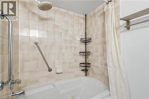 Tiled shower surround with a corner tub featuring a shower head and grab bars - 175 Hunter Street E Unit# 401, Hamilton, ON - Indoor Photo Showing Bathroom