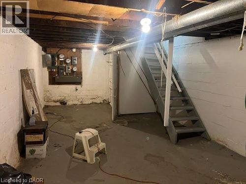 Unfinished basement space featuring exposed ceiling joists, painted concrete block walls, a concrete floor, an electrical panel, and an open staircase - 194 Kenilworth Avenue N, Hamilton, ON 