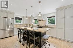 Kitchen featuring a central island with seating, pendant lighting, stainless steel appliances, light-toned cabinetry, and tile flooring - 