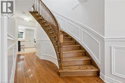 Curved wooden staircase with balusters, wood-finish flooring, white wainscoting, and recessed lighting - 