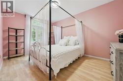 Bedroom featuring light wood-finish flooring, a large arched window with white curtains, and soft pink walls - 