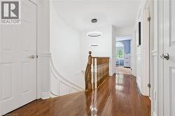 Hallway featuring hardwood flooring, white paneled doors, and a natural wood staircase railing - 