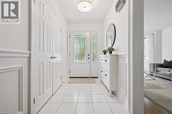 Foyer featuring a white entry door with decorative glass inserts, crisp white paneling, square tile flooring, and a semi-flush mount ceiling light - 