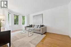 Bright living space featuring a bay window, wood-finish flooring, and crisp white walls - 