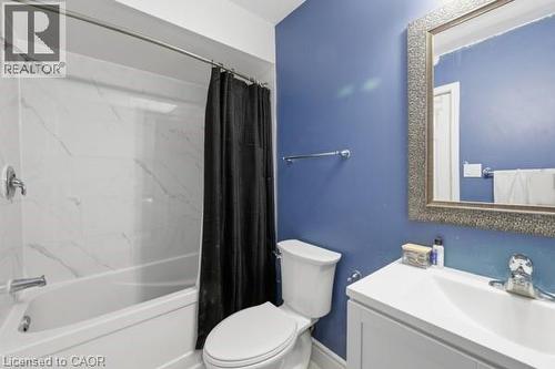 Bathroom featuring a white vanity with integrated sink, a framed mirror, and a toilet - 16 Harrison Avenue, Hamilton, ON 