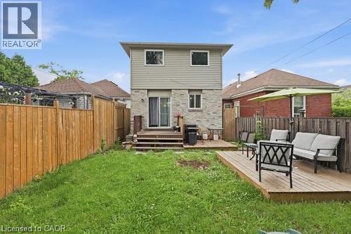Private backyard space featuring a multi-level deck, wood fencing, and a grassy area - 16 Harrison Avenue, Hamilton, ON 